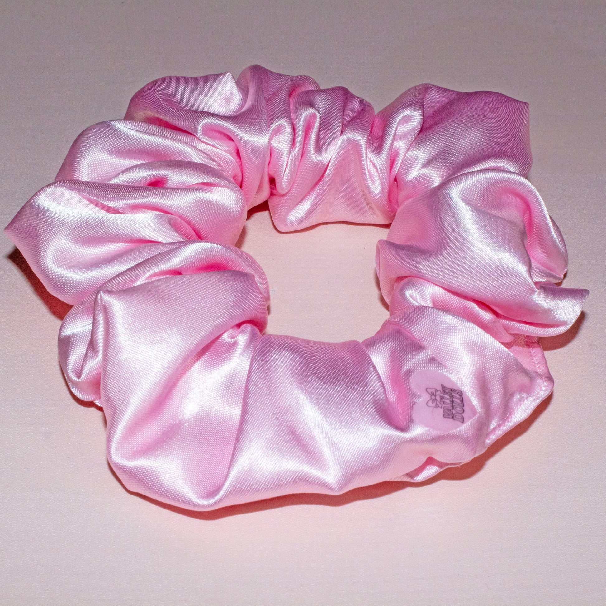 Pink satin scrunchie with a smooth glossy finish, handmade hair accessory displayed on a neutral background
