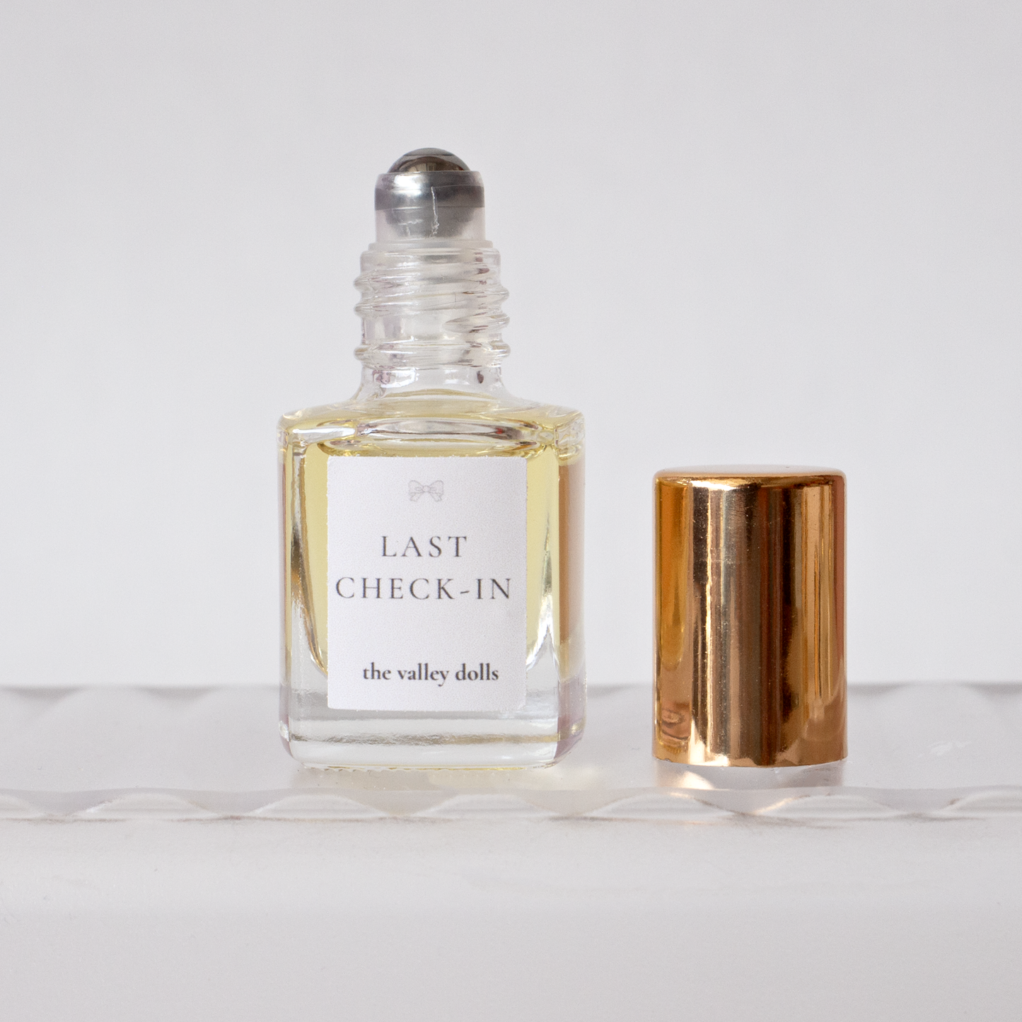 Open luxury perfume oil bottle labeled “Last Check-In” with exposed roller applicator on a white background