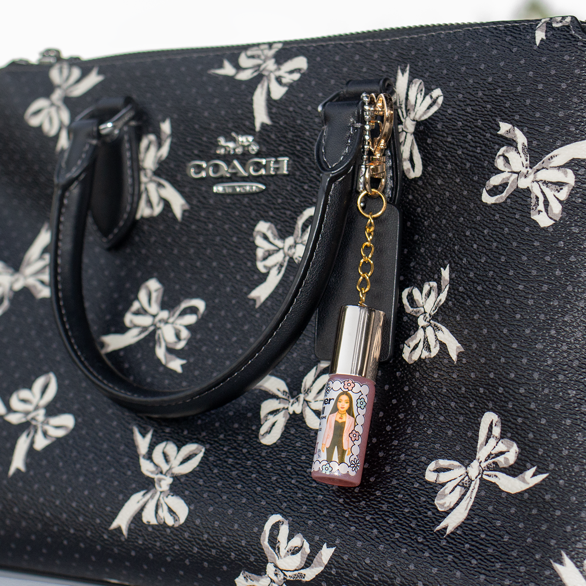 Power Doll perfume oil roll-on in 5ml glass bottle with gold heart keychain clasp attached to black bow-print handbag