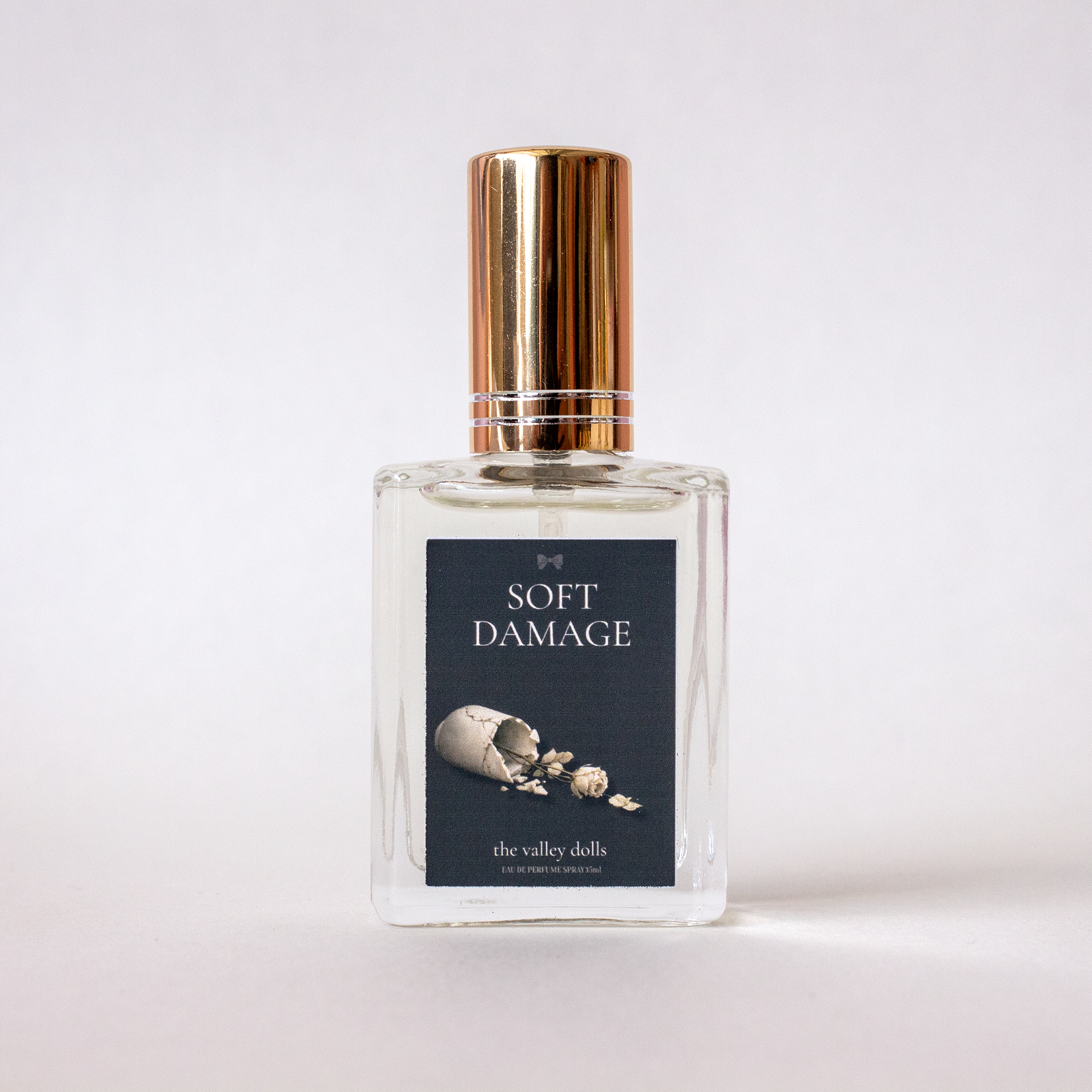 Luxury perfume bottle labeled “Soft Damage” with gold cap and soft blue label on a white background