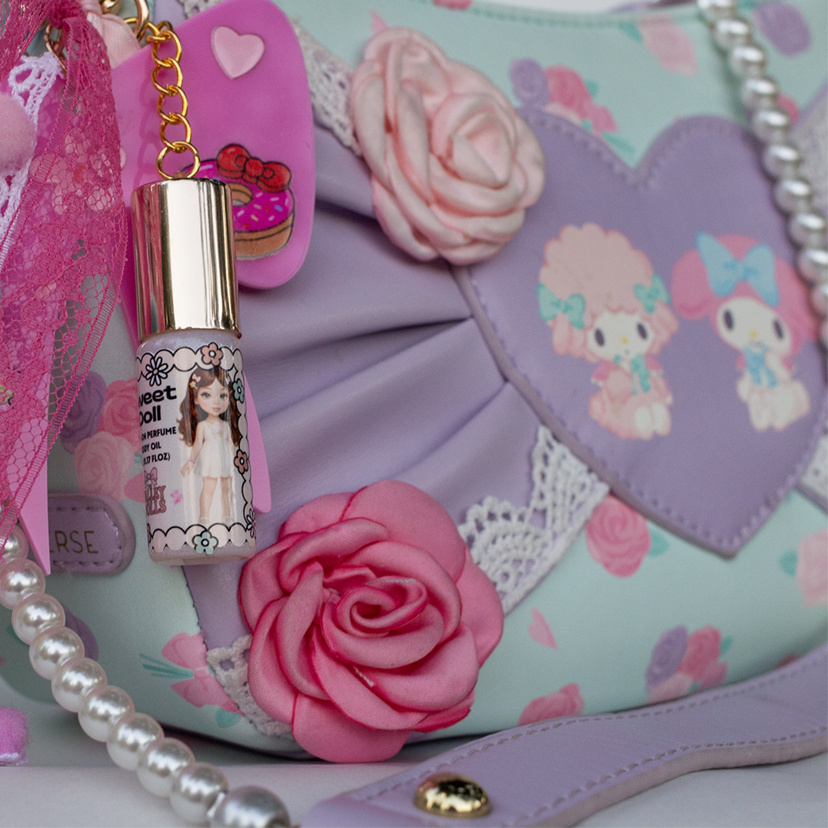 Sweet Doll perfume oil roll-on in 5ml glass bottle with gold heart keychain clasp, styled on pastel purse with floral details