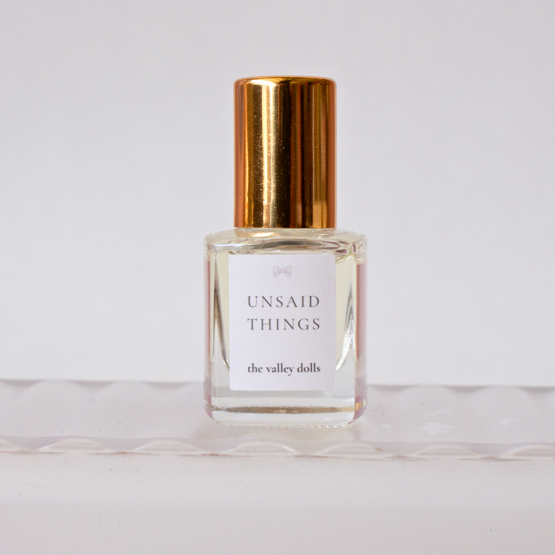 Luxury perfume oil bottle labeled “Unsaid Things” with gold cap on a white background
