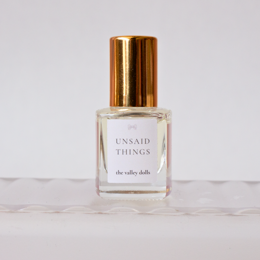 Luxury perfume oil bottle labeled “Unsaid Things” with gold cap on a white background