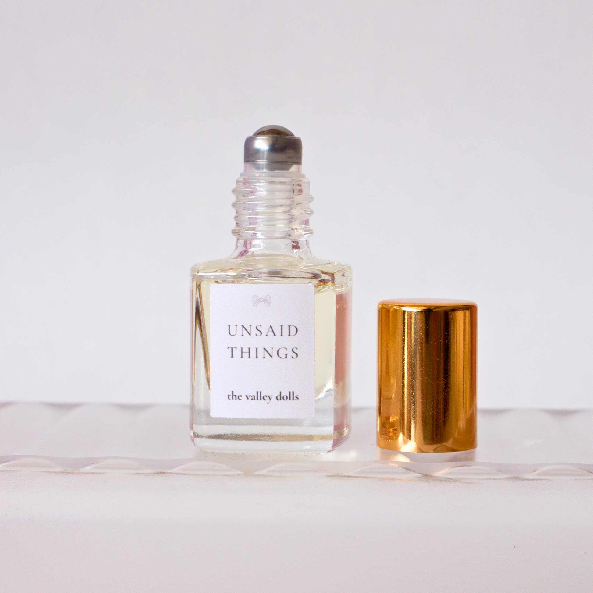 Open luxury perfume oil bottle labeled “Unsaid Things” with exposed roller applicator on a white background