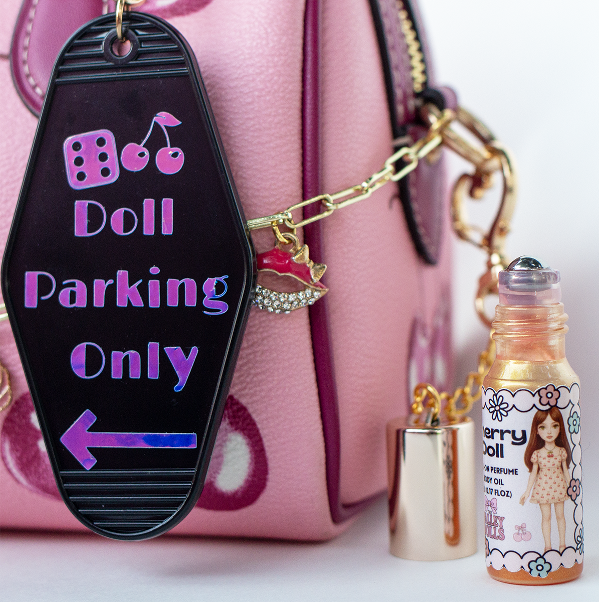 The Valley Dolls Doll Parking Only motel keychain with open Cherry Doll perfume oil bottle lifestyle shot