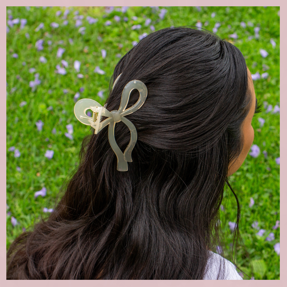 Clear  bow hair clip in dark hair, The Valley Dolls accessory, outdoor grass background