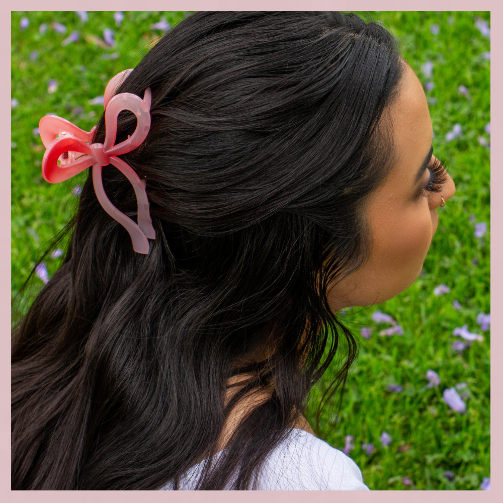 Pink ribbon hair bow clip in dark hair, The Valley Dolls accessory, outdoor grass background
