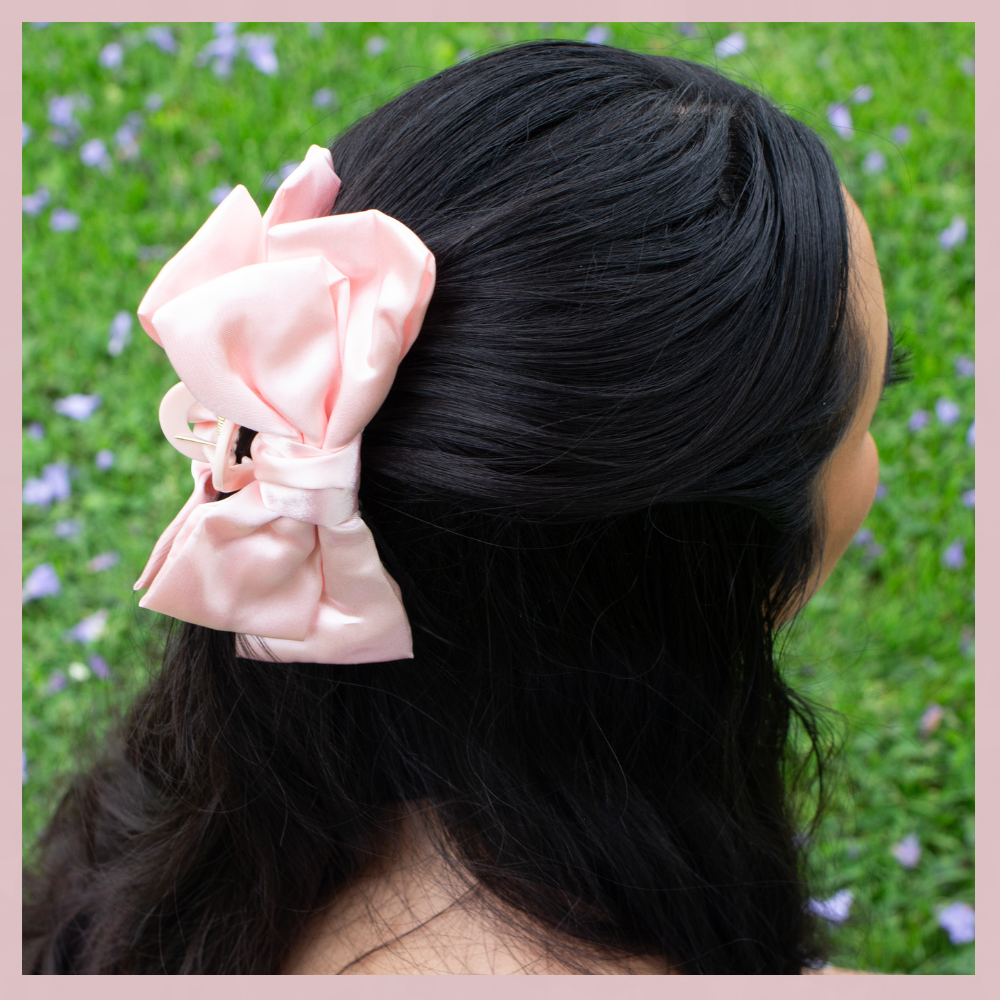 Soft pink satin bow hair clip in dark hair, The Valley Dolls accessory, outdoor grass background
