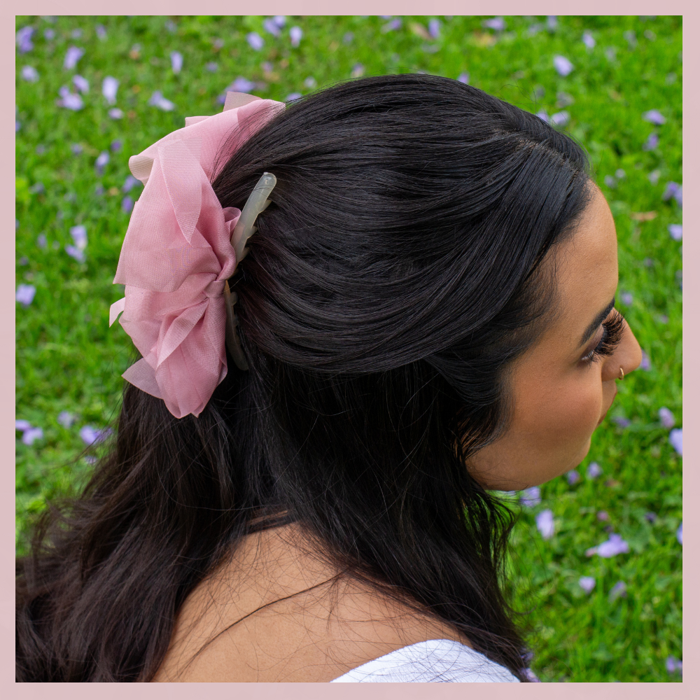 Pink mesh bow hair clip in dark hair, The Valley Dolls accessory, outdoor grass background